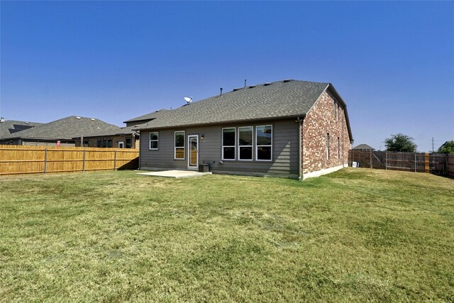 back of house with a lawn, a patio, a fenced backyard, roof with shingles, and brick siding