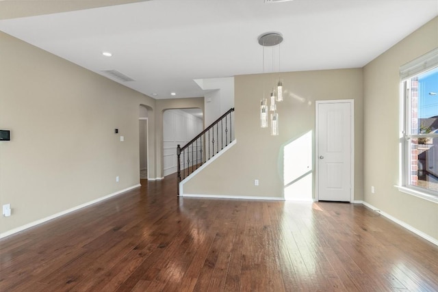 spare room with hardwood / wood-style flooring, stairs, baseboards, and arched walkways