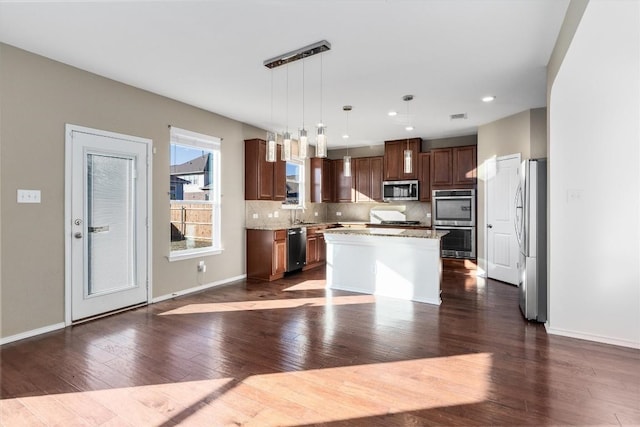 kitchen with tasteful backsplash, a kitchen island, appliances with stainless steel finishes, dark wood-type flooring, and hanging light fixtures