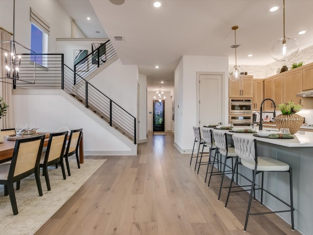 kitchen featuring light wood-type flooring, pendant lighting, light brown cabinetry, a notable chandelier, and double oven