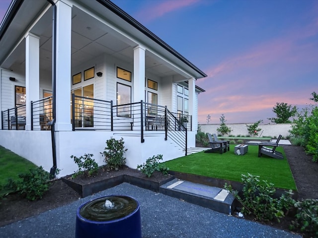 property exterior at dusk featuring a yard, a fire pit, and a porch