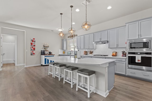 kitchen featuring a breakfast bar area, a kitchen island with sink, light hardwood / wood-style flooring, pendant lighting, and stainless steel appliances