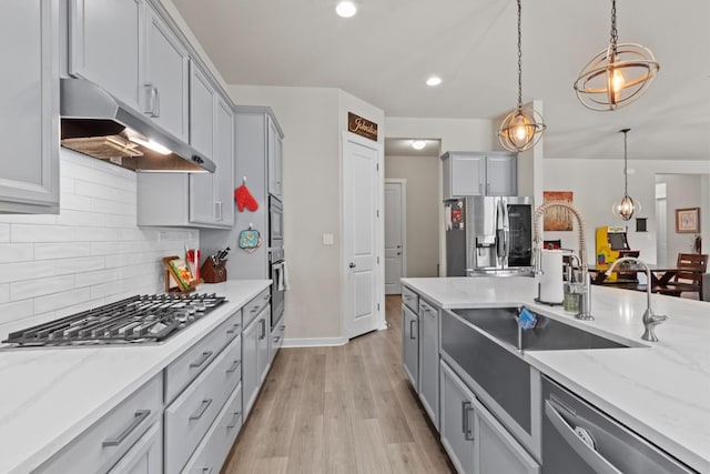 kitchen with gray cabinetry, sink, pendant lighting, light wood-type flooring, and appliances with stainless steel finishes