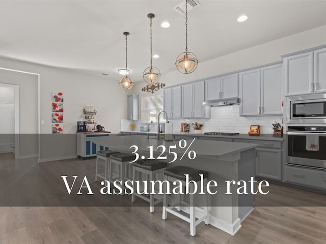 kitchen featuring appliances with stainless steel finishes, dark hardwood / wood-style floors, and an island with sink