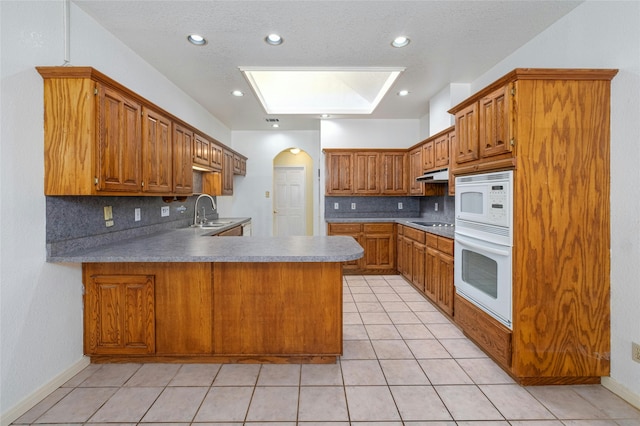 kitchen featuring decorative backsplash, sink, white appliances, and kitchen peninsula