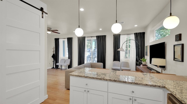 kitchen with light stone counters, open floor plan, pendant lighting, light wood-style flooring, and white cabinetry