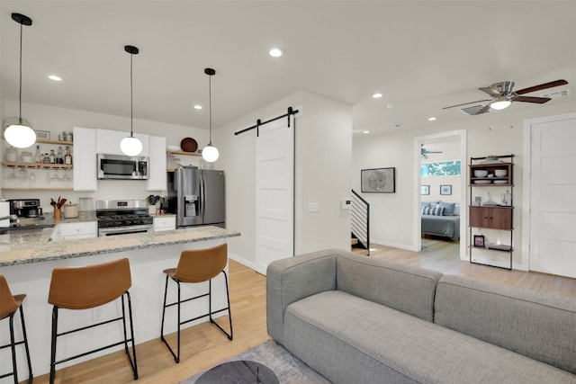 kitchen featuring stainless steel appliances, a barn door, open floor plan, light wood-style floors, and a kitchen bar