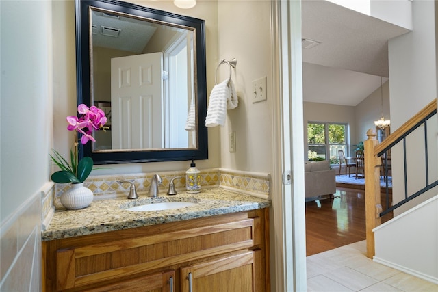 bathroom featuring an inviting chandelier, a textured ceiling, vaulted ceiling, vanity, and hardwood / wood-style flooring