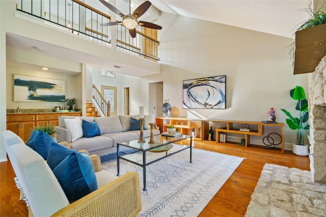 living room featuring light wood-type flooring, ceiling fan, sink, beam ceiling, and high vaulted ceiling