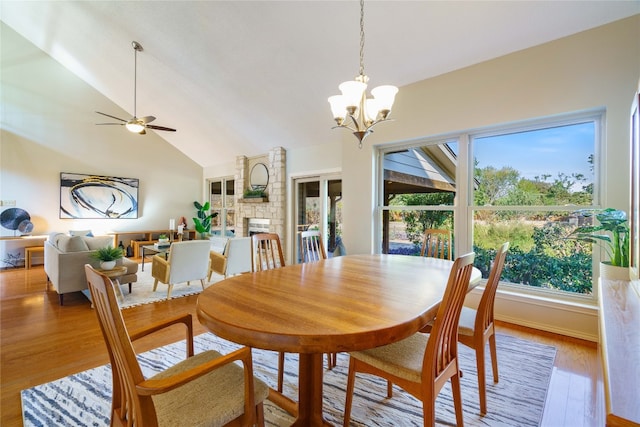 dining area with lofted ceiling, light wood-type flooring, a fireplace, and ceiling fan with notable chandelier