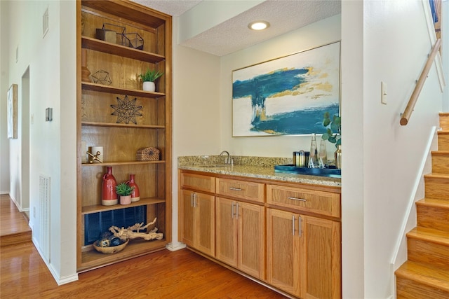 bar featuring light stone countertops, hardwood / wood-style floors, a textured ceiling, and sink