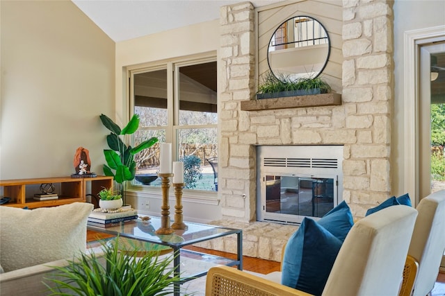 living room featuring hardwood / wood-style flooring, a stone fireplace, and vaulted ceiling