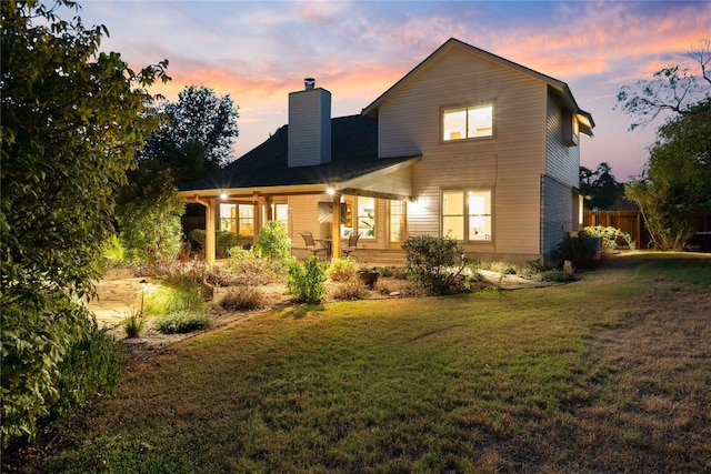 back house at dusk featuring a lawn