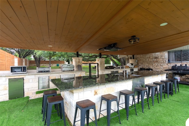 view of patio with an outdoor kitchen, area for grilling, ceiling fan, and a wet bar