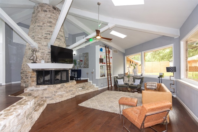 living room with ceiling fan, a stone fireplace, dark wood-type flooring, and lofted ceiling with skylight