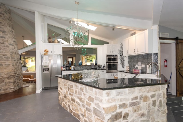 kitchen with stainless steel appliances, white cabinets, kitchen peninsula, a barn door, and vaulted ceiling with skylight