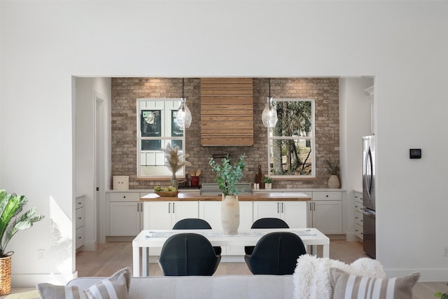 kitchen featuring white cabinets, hanging light fixtures, decorative backsplash, stainless steel fridge, and light wood-type flooring