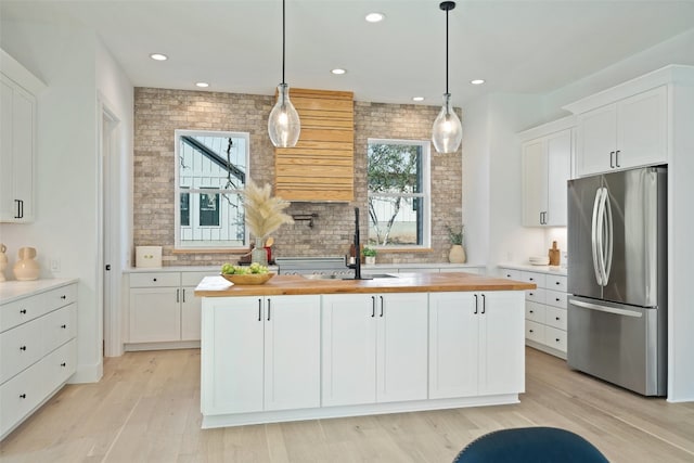 kitchen with stainless steel refrigerator, white cabinetry, an island with sink, and wooden counters