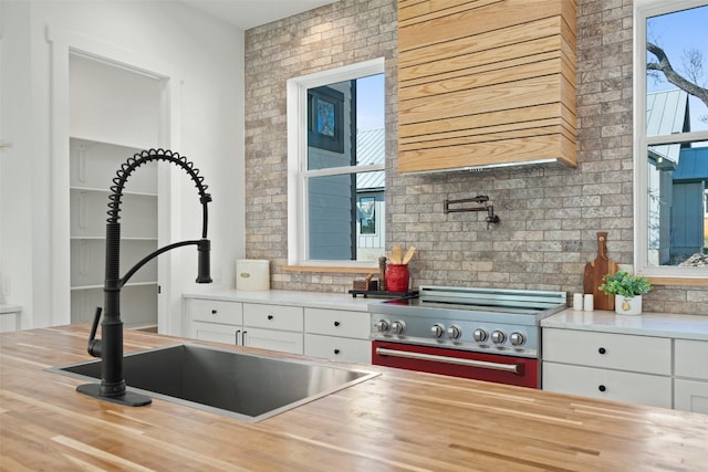 kitchen with sink, high end stove, butcher block countertops, decorative backsplash, and white cabinets