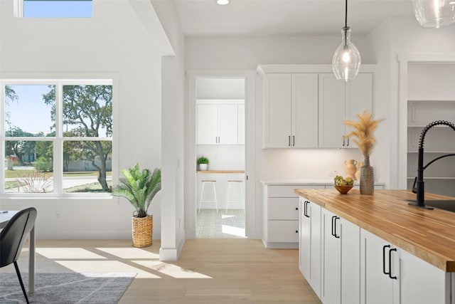 kitchen featuring sink, decorative light fixtures, light hardwood / wood-style floors, white cabinetry, and butcher block counters