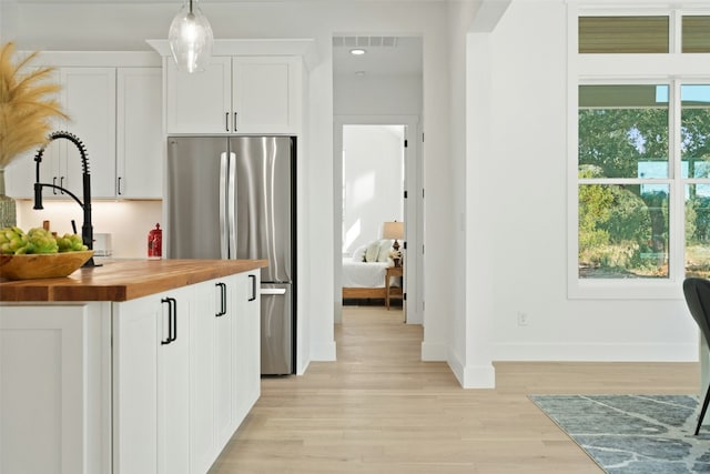 kitchen featuring stainless steel refrigerator, white cabinetry, sink, butcher block countertops, and pendant lighting