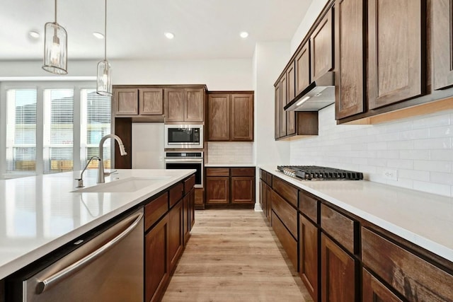 kitchen with pendant lighting, sink, decorative backsplash, appliances with stainless steel finishes, and light hardwood / wood-style floors