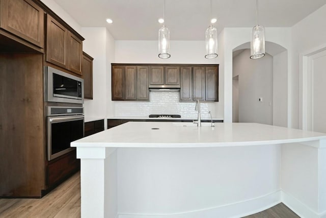 kitchen featuring a center island with sink, light hardwood / wood-style flooring, decorative light fixtures, and appliances with stainless steel finishes