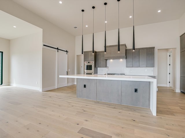 kitchen featuring oven, light wood-type flooring, a barn door, a spacious island, and decorative light fixtures