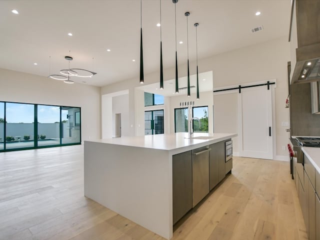 kitchen with a spacious island, a barn door, light wood-type flooring, pendant lighting, and sink