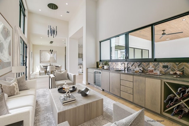 living room with sink, ceiling fan, a high ceiling, beverage cooler, and light hardwood / wood-style flooring