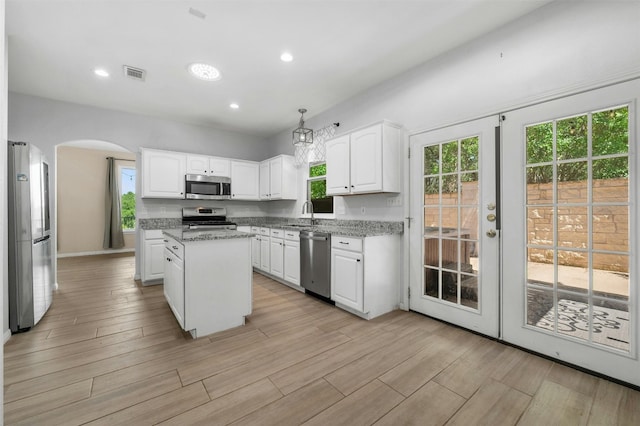 kitchen with appliances with stainless steel finishes, decorative light fixtures, white cabinets, a center island, and light stone countertops