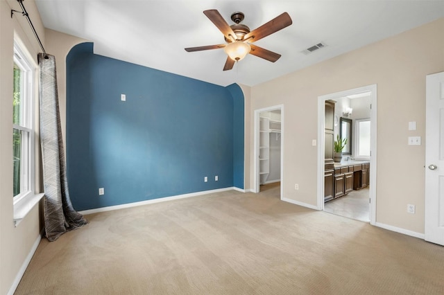 interior space featuring multiple windows, a spacious closet, ensuite bath, and light colored carpet