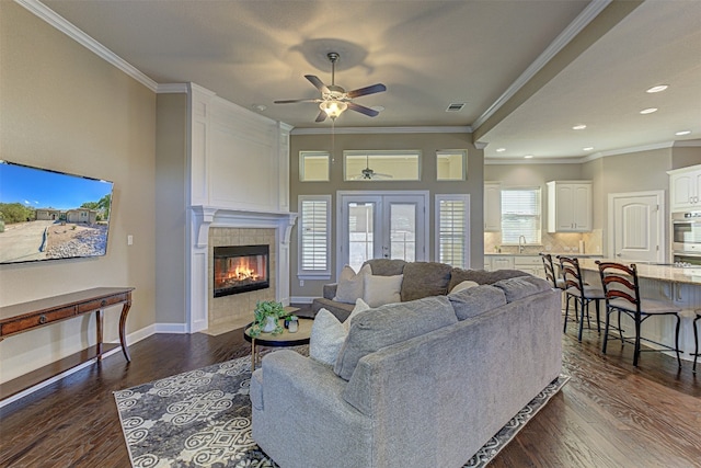 living room featuring a tile fireplace, dark hardwood / wood-style floors, ceiling fan, and crown molding