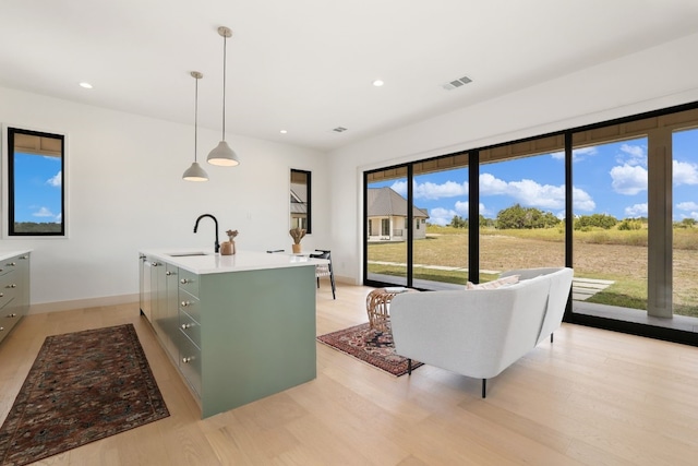 kitchen featuring decorative light fixtures, a kitchen island with sink, sink, and light hardwood / wood-style flooring