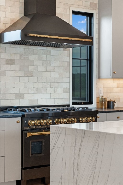 kitchen with white cabinets, wall chimney exhaust hood, backsplash, and high end stove