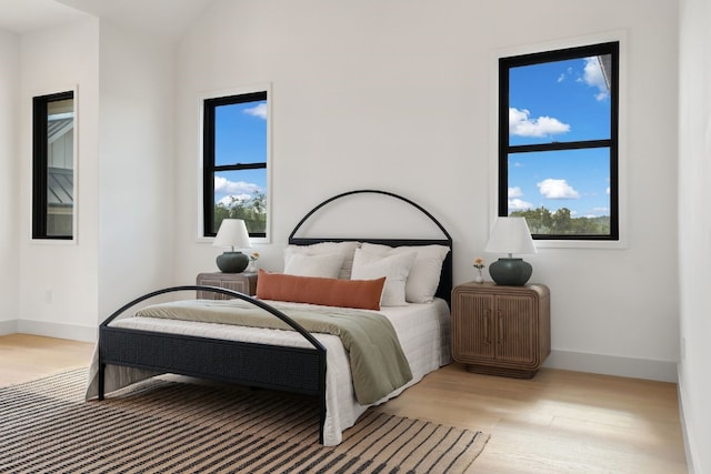 bedroom featuring light hardwood / wood-style flooring, vaulted ceiling, and multiple windows