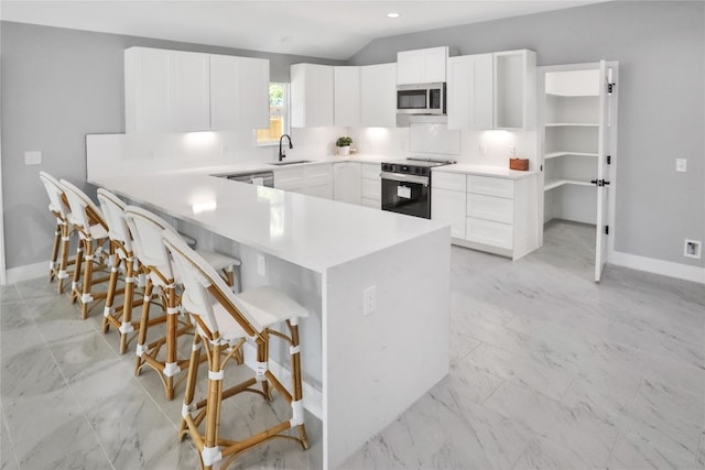 kitchen featuring sink, white cabinetry, vaulted ceiling, appliances with stainless steel finishes, and a kitchen breakfast bar