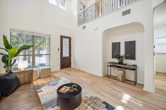 living room with a towering ceiling, plenty of natural light, and light wood-type flooring