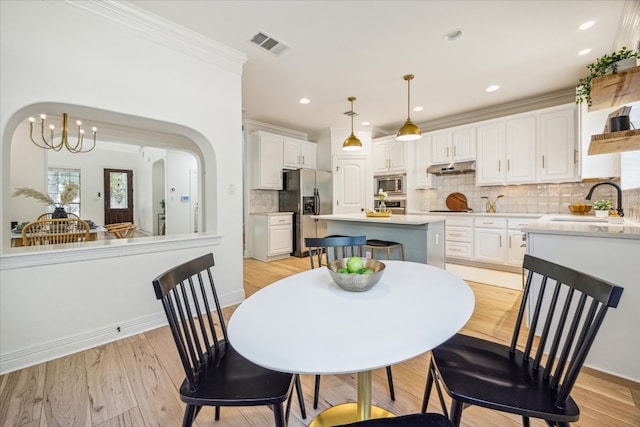 dining room with crown molding, sink, light wood-type flooring, and a chandelier