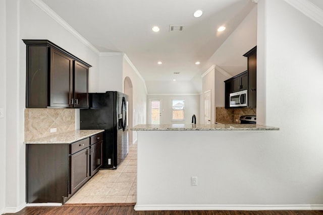 kitchen with appliances with stainless steel finishes, kitchen peninsula, light stone counters, and light hardwood / wood-style floors