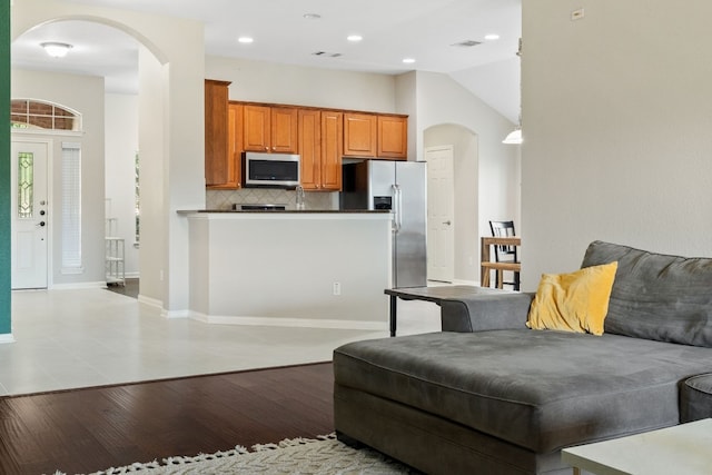 kitchen featuring kitchen peninsula, tasteful backsplash, stainless steel appliances, vaulted ceiling, and light hardwood / wood-style flooring