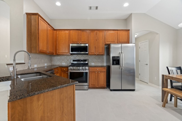 kitchen featuring sink, stainless steel appliances, backsplash, kitchen peninsula, and dark stone countertops