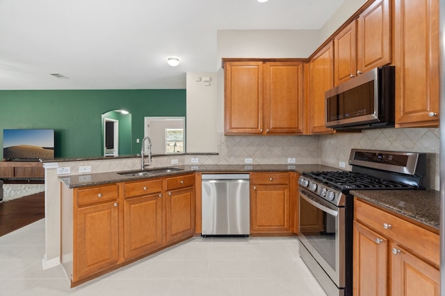 kitchen featuring appliances with stainless steel finishes, tasteful backsplash, dark stone counters, sink, and light tile patterned flooring