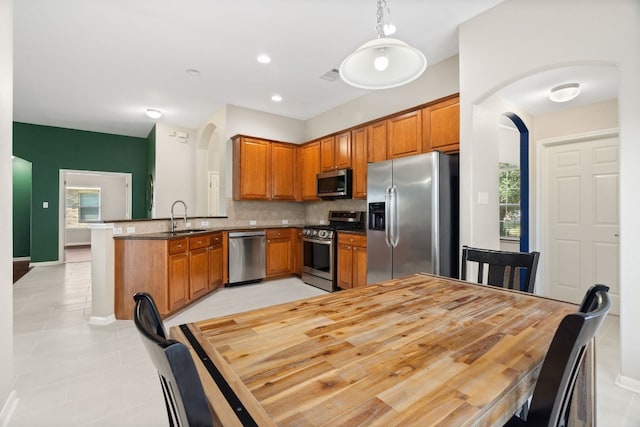 kitchen with kitchen peninsula, backsplash, stainless steel appliances, sink, and hanging light fixtures