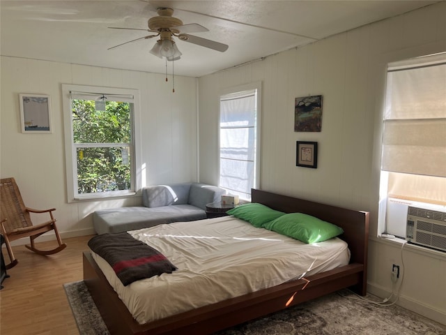 bedroom featuring wood walls, cooling unit, light hardwood / wood-style flooring, and ceiling fan