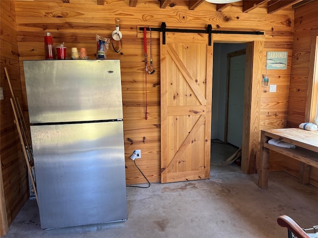 kitchen featuring fridge, a barn door, wood walls, and concrete floors