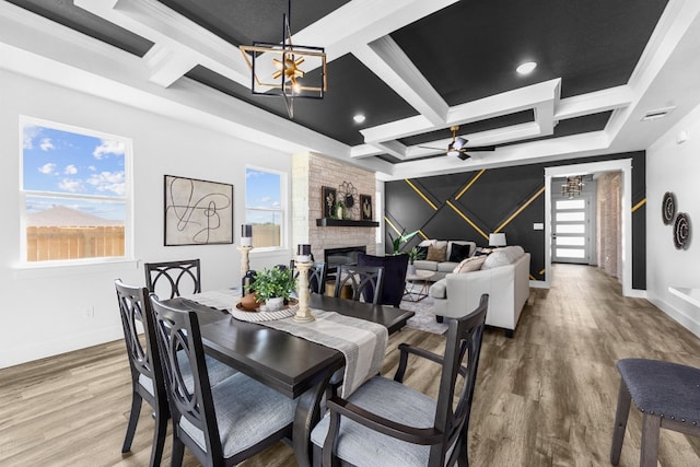 dining space featuring a large fireplace, wood-type flooring, coffered ceiling, and a wealth of natural light