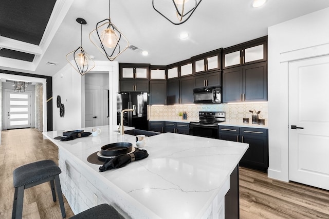 kitchen with black appliances, dark brown cabinetry, a kitchen island with sink, light hardwood / wood-style flooring, and decorative light fixtures