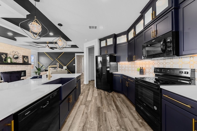 kitchen with light wood-type flooring, black appliances, sink, a fireplace, and hanging light fixtures