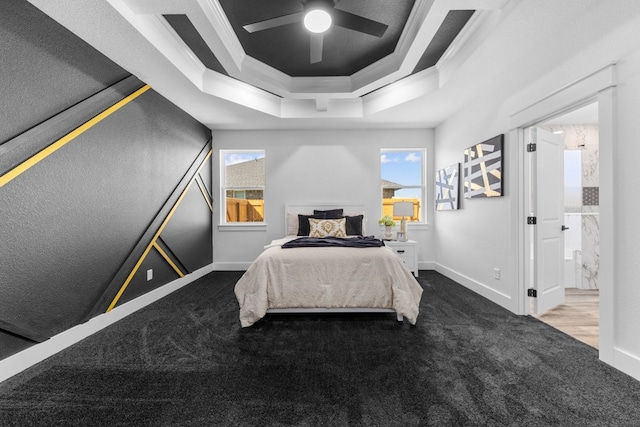 bedroom with ceiling fan, a raised ceiling, dark colored carpet, ensuite bath, and ornamental molding